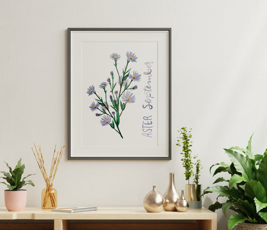 A picture frame featuring the Aster flower floats above a shelf with gold knick knacks and an assortment of house plants.